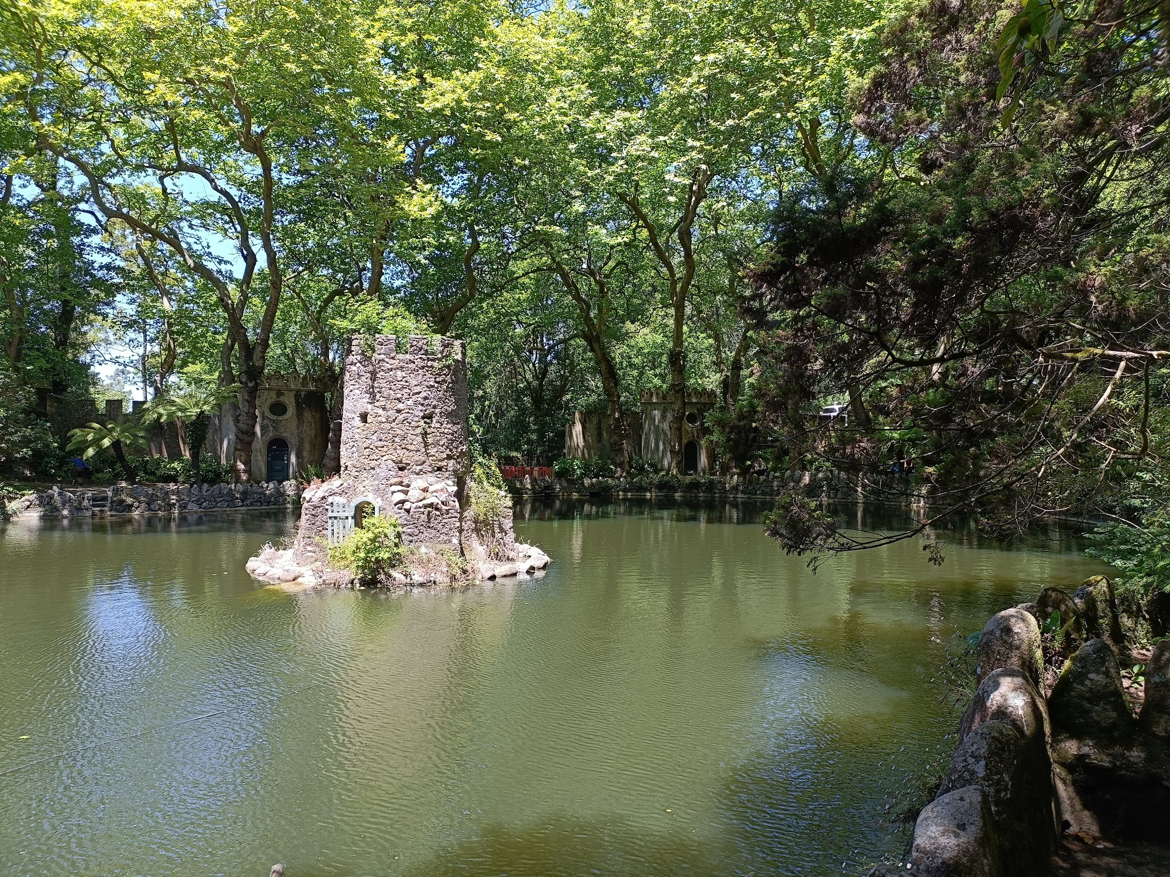 A pond with a tiny island in the middle which has a large duck house in the shape of a tower.